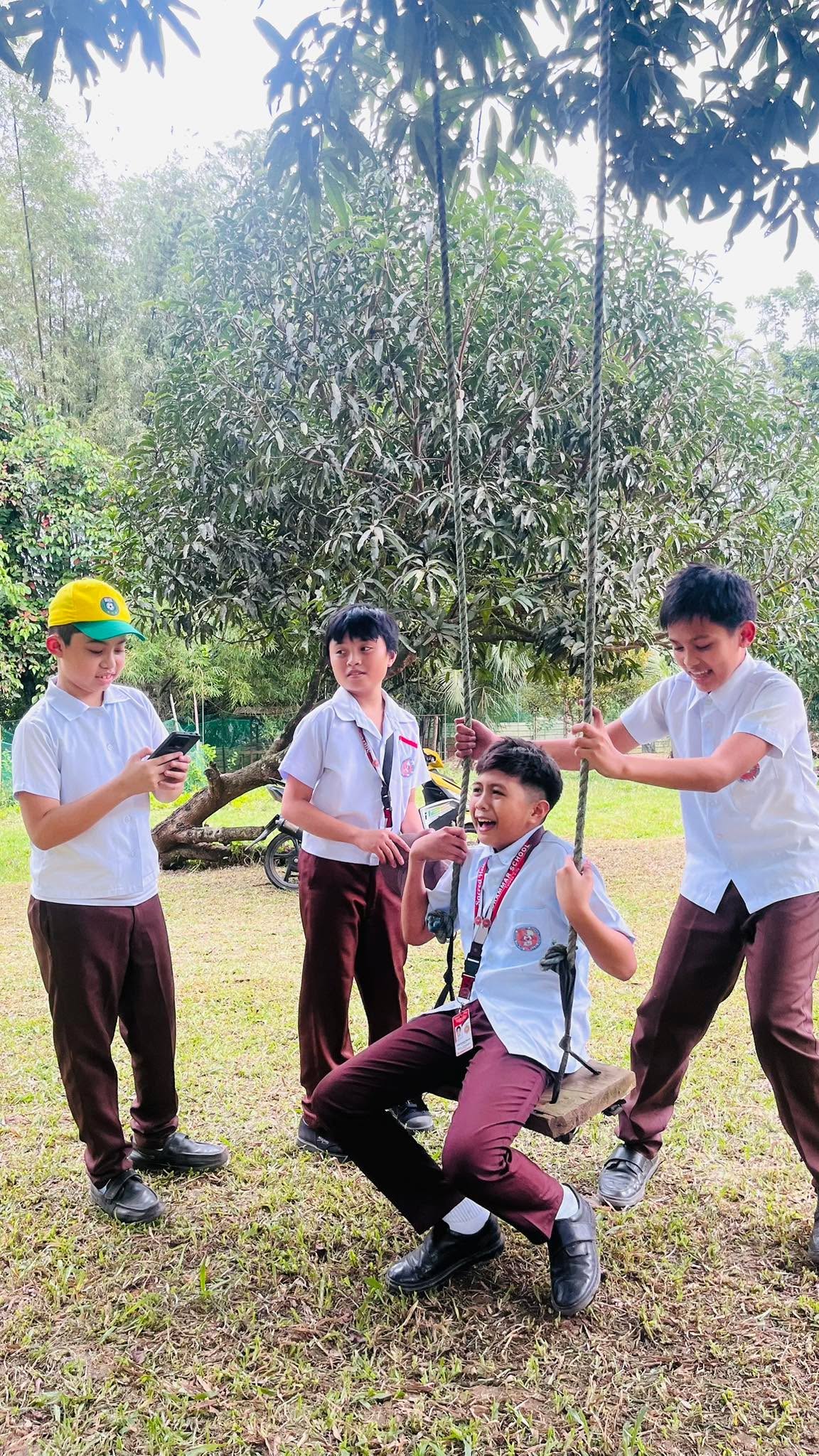 Sacred Heart students in formal school uniforms laughing together at a swing